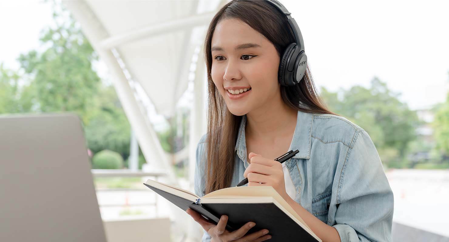 woman in jackat and wearing headphones on writing notes down 